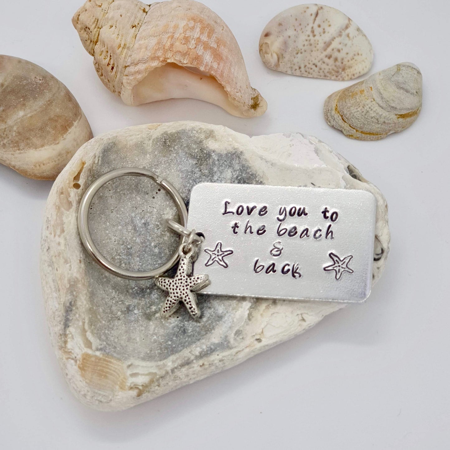 Rectangular keyring with the words 'I love you to the beach and back' hand stamped along with two starfish stamps and a starfish charm.